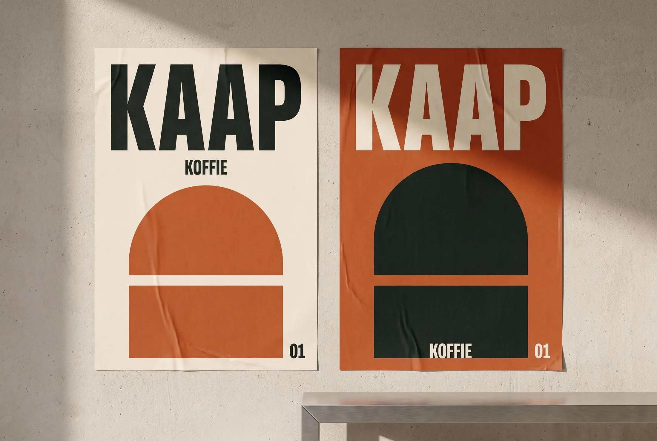 Twee KAAP-posters in crème en roestoranje op een lichte betonnen muur, met grote letters en onderbroken bogen.